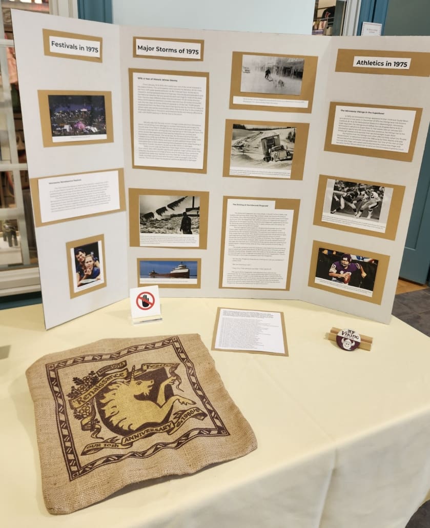 This trifold displays the info from the sections about Minnesota events around 1975 including the Vikings in the superbowl, the founding of the MN Reniassance fair, the sinking of the Edmund Fitzgerald, and the massive winter storms. In front is two artifacts. One is an original MN Ren faire tote bag made of twine/potato sack material with the original unicorn crest on it, thee second is a vintage vikings fan club pin.