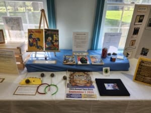 This picture includes the objects from the pop culture section as well as the Taco Daze highlight section. The Taco Daze section includes catalouged objects from past years such as an old newspaper, old memory book with photos inside, a taco paper craft, and hand made meatball jiggly headbands that volunteers would wear to sell tickets.